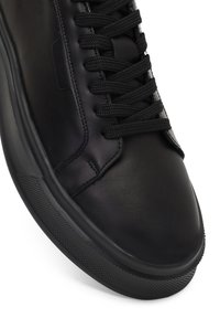 Sneaker in pelle nera con suola in gomma testurizzata, punta rotonda e lacci neri piatti. I dettagli delle cuciture aggiungono dimensione alla superficie liscia.