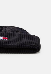 Gorro de malha azul-escuro com uma dobra larga canelada e um patch de logótipo com riscas vermelhas e brancas de um lado.