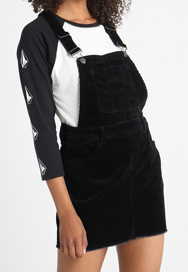 Svart kordflodoverallklänning med justerbara remmar, framficka och rå kant. Kombinerad med en svart och vit långärmad topp.