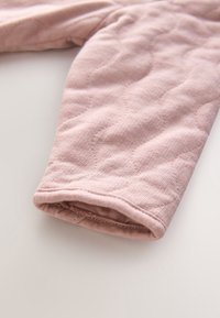 Manche en tissu matelassé rose avec une texture douce, montrée en gros plan sur une surface claire.
