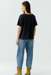 Black short-sleeve top with a relaxed fit, paired with light blue tapered jeans and tan suede ankle boots. Smooth fabric, minimal design.