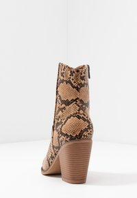 Heeled ankle boot in a beige and brown snakeskin pattern, featuring a textured surface and a brown stacked heel. Zipper detail on the side.