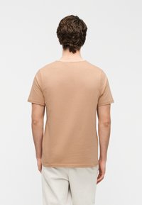 Κοντομάνικο t-shirt με στρογγυλή λαιμόκοψη σε ανοιχτό μπεζ βαμβάκι. Λείο ύφασμα, μίνιμαλ σχεδιασμός χωρίς ορατά λογότυπα ή μοτίβα.