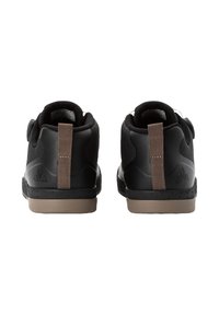 Baskets noires avec une tige en maille texturée, un talon rond et une languette brun à l'arrière. Semelle en caoutchouc grise avec de petites perforations.