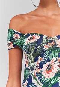 Niebieski, kwiecisty bodysuit na ramiączkach z różowymi i zielonymi tropikalnymi wzorami. Wykonany z miękkiego materiału, z marszczonymi rękawami i dopasowanym krojem.