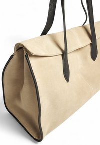 Bežinis suedinės rankinės krepšys su juodais odiniais akcentais, stačiakampio formos, dviem ilgomis rankenomis ir užlenkiamu dangteliu viršuje.