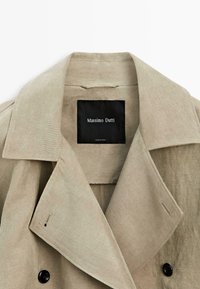 Beige linned trenchcoatkrave og slag med sort "Massimo Dutti" mærke syet ind i nakken.