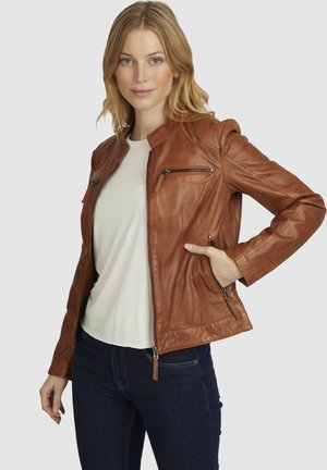Braune Lederjacke mit Stehkragen, Reißverschlusstaschen und taillierter Passform. Über einem hellen Hemd getragen und mit dunklen Jeans kombiniert.