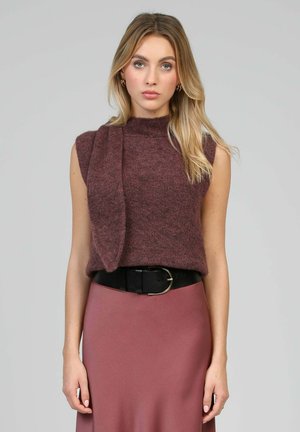 Pull sans manches en maille de couleur mauve profond avec un col montant, associé à une jupe en satin rose élégante et une ceinture noire avec une boucle en métal.