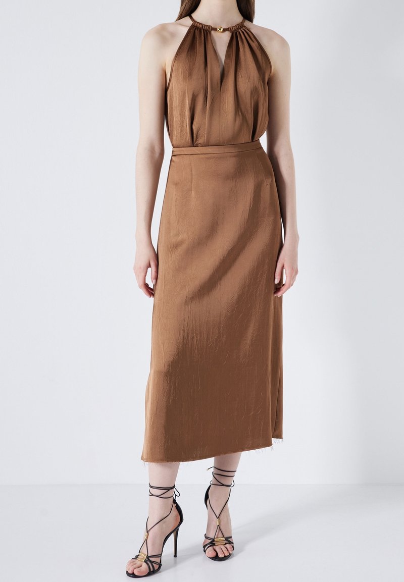 Robe brune à col halter avec un bustier plissé, une silhouette fluide et une longueur mi-mollet ; associée à des sandales à talons hauts noires à lanières.
