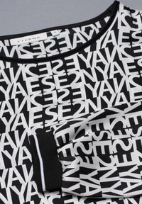 Svart och vit topp med ett mönster av text över hela. Rund halsringning med svart kant. Ärmslut har svart tyg med vit randdetalj.