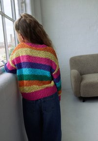 Colorful knitted sweater featuring striped patterns in orange, pink, purple, turquoise, and green; textured design, paired with denim.