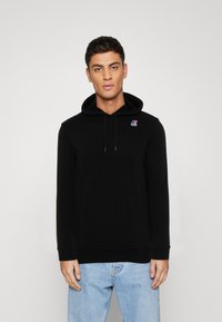 Felpa nera con cappuccio regolabile, polsini e orlo a costine. Presenta un piccolo logo sul petto. Il materiale appare morbido e testurizzato.