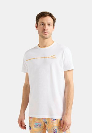 Uomo che indossa una maglietta bianca con una piccola grafica arancione e testo sul petto e pantaloncini arancioni con fantasia.