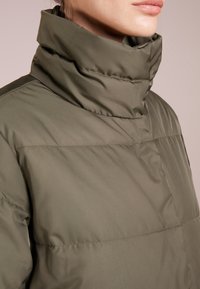 Olivgrüne Pufferjacke mit hohem Kragen, ausgestattet mit gesteppten Paneelen und einer glatten, glänzenden Textur. Keine sichtbaren Hardware-Elemente oder Akzente.