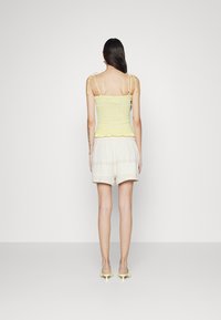 Top amarelo franzido com laços nos ombros, combinado com calções claros e estampados. O top tem um hem rufado, e os calções são folgados com uma cintura elástica.
