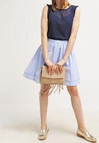 Marinblå texturerad ärmlös topp, ljusblå utställd kjol, beige clutch med fransdetaljer och metalliska loafers. Enkelt, avslappnat plagg.