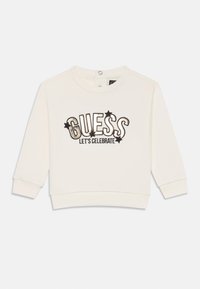 Sweatshirt blanc à manches longues, col rond, présentant le texte brodé en noir et or "GUESS LET'S CELEBRATE" et des accents d'étoiles.