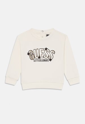 Valge pikkade varrukatega sweatshirt ümmarguse kaelusega, millel on musta ja kuldse tikandiga tekst "GUESS LET'S CELEBRATE" ja tähtede aksendid.