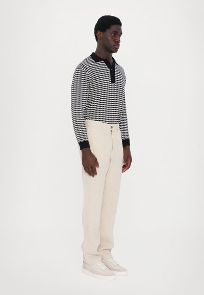 Navy and white patterned long-sleeve polo shirt, beige linen trousers, and light sneakers. Soft texture, relaxed fit, contrasting collar.