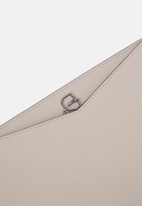 Bežová kožená kabelka typu clutch s metalickou siluetu loga částečně viditelnou uvnitř trojúhelníkové kapsy.