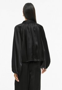 Černá saténová halenka s vysokým límcem, zády s plisovaným detailem a balónovými rukávy. Hladká textura a volný střih.