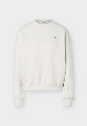 Λευκό μακρυμάνικο φούτερ με στρογγυλή λαιμόκοψη, ριμπ μανσέτες και τελείωμα, μικρό μαύρο λογότυπο στο αριστερό στήθος και διακριτική λεπτομέρεια στη ραφή στο πλάι.