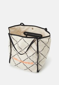 Torba typu tote w kremowym płótnie z czarnymi detalami, z diamentowym wzorem tekstu "KARL LAGERFELD" oraz wewnętrzną kieszenią na zamek do przechowywania.