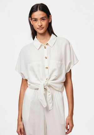 Hvid, kortærmet skjorte lavet af letvægts stof, med krave, knaplukning, to brystlommer og en knude bundet om taljen.