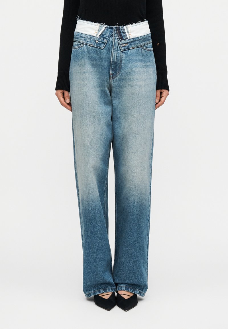 Jeans albastru deschis, cu picioare largi și talie albă cu margini tocite, având un design clasic cu cinci buzunare și o spălare ușor estompată. Include tocuri negre.