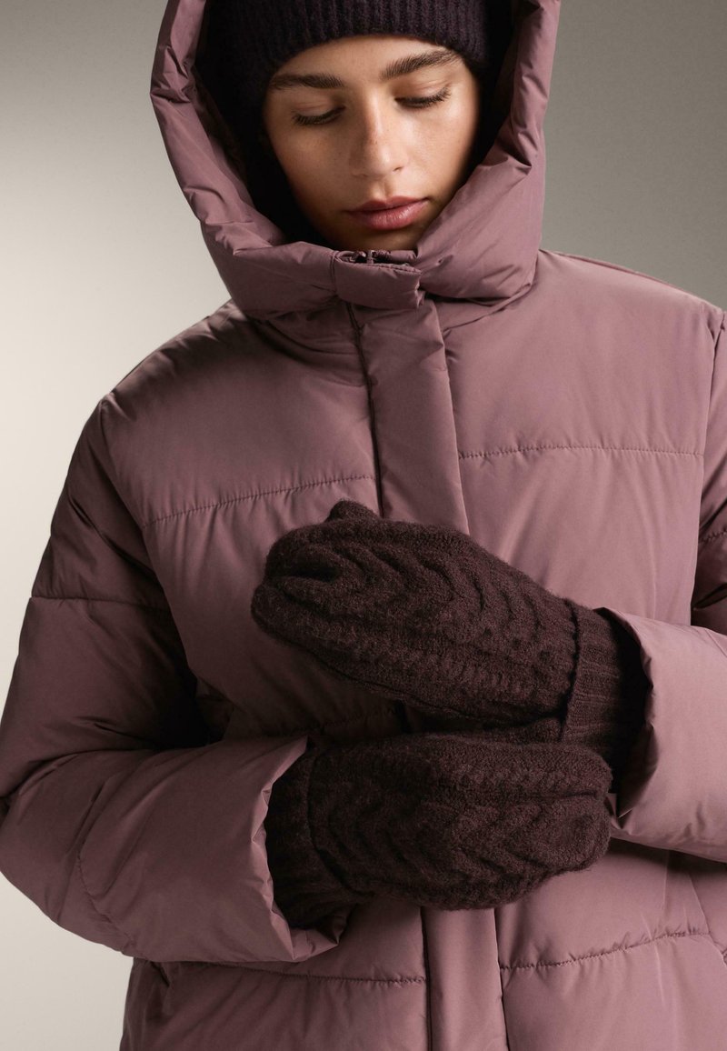 Geacă matlasată mauve cu guler înalt, asortată cu mănuși tricotate maro închis cu un model texturat. Material neted cu izolație caldă.