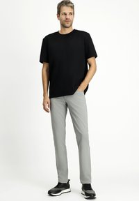 T-shirt nera a maniche corte, pantaloni grigi e sneakers nere. La T-shirt ha una vestibilità rilassata; i pantaloni sono slim con tasche e una texture liscia.