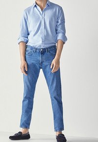 Vaaleansininen nappikuvioinen paita, käännetyt hihat, tummansiniset farkut, slim fit -malli ja tummat kengät, joissa on rusetti. Yksinkertainen muotoilu, rento ilme.