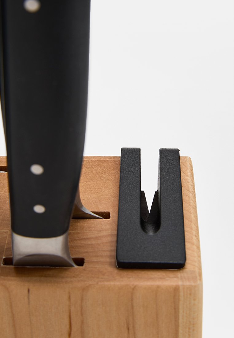 Couteau inséré dans un bloc en bois à côté d'une fente de fusil à aiguiser noire sur fond blanc.