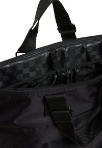Sac fourre-tout noir avec une fermeture éclair, doté d'un intérieur texturé avec un motif à carreaux et plusieurs poches intérieures pour une meilleure organisation.