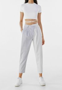 Bílý crop top s křížkovými ramínky, spárovaný se šedými kalhotami s kostkovaným vzorem na jedné straně a svislými pruhy na druhé.