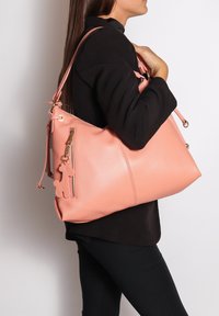 Borsa a tracolla in pelle rosa con finitura testurizzata, dotata di una tasca con zip e di un ciondolo decorativo. Tracolla regolabile e forma arrotondata.