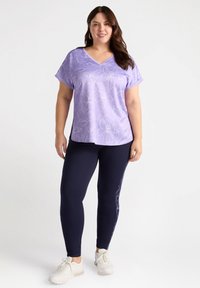 Lilla blomstrede V-hals top lavet af blødt stof, parret med marineblå leggings med blomsterdesign langs siden, suppleret med hvide sneakers.