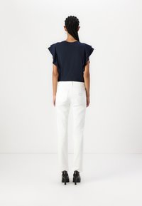 Camiseta azul marino con mangas acampanadas, combinada con pantalones rectos blancos y tacones negros, con detalles de costura sutil en la parte posterior de los pantalones.