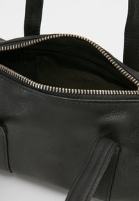 Czarna skórzana torba na ramię z zamkiem błyskawicznym, o gładkiej fakturze, z podwójnymi uchwytami i wewnętrzną metką z logo.