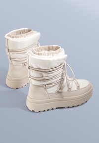 Bézs színű, bélelt csizma párnázott, elasztikus felsőrésszel, fűzős elülső résszel és texturált gumitalppal. Sima anyag matt felülettel.