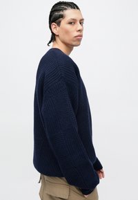 Maglione lavorato a maglia blu navy con motivi testurizzati, maniche lunghe e vestibilità comoda. Il tessuto appare spesso e accogliente, con orlo a coste.