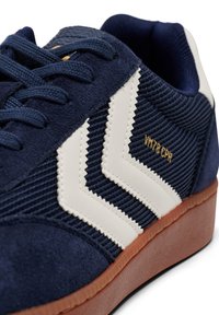 Navy blue sneaker with white chevron stripes, suede and textured fabric, rubber sole, and gold "VM78 CPH" detail on the side.