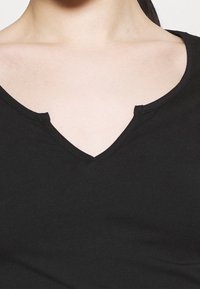 Musta t-paita, jossa on V-kaula-aukko, pehmeä rakenne ja yksinkertainen kangas ilman kuvioita tai koristeluja. Yksinkertainen ja tiukka muotoilu.
