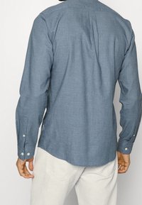 Camicia azzurro chiaro a maniche lunghe realizzata in tessuto testurizzato. Presenta un polsino con bottoni e un orlo curvo. La parte posteriore ha una piega centrale.