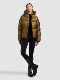 Olívazöld, kapucnis pehelykabát cipzáras záródással, rugalmas mandzsettákkal és varrott részletekkel, fekete leggingsszel és csizmával párosítva.