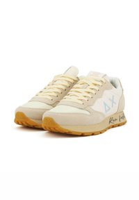 Beige Sportschuhe mit Obermaterial aus Wildleder und Mesh, hellblauem Logo und Akzenten, gelber Gummisohle und einem bedruckten "Schneller laufen"-Detail.