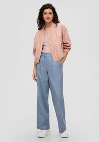 Helle rosa Bomberjacke mit elastischen Bündchen, kombiniert mit weit geschnittenen hellblauen Hosen. Weiße Sneakers runden das Outfit ab.