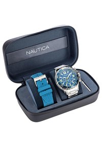 Nautica pulkstenis iestatīts melnā ar rāvējslēdzēju aizvērtā kastē, ar zilu ciparnīcu un sudraba akcentiem. Ietver zilu gumijas jostu un sudraba metāla rokassprādzi.