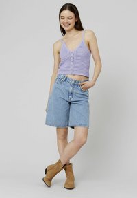 Top cropped lavande avec des boutons à l'avant et une texture en tricot, associé à un short en jean bleu clair. Des bottines marron complètent l'ensemble.